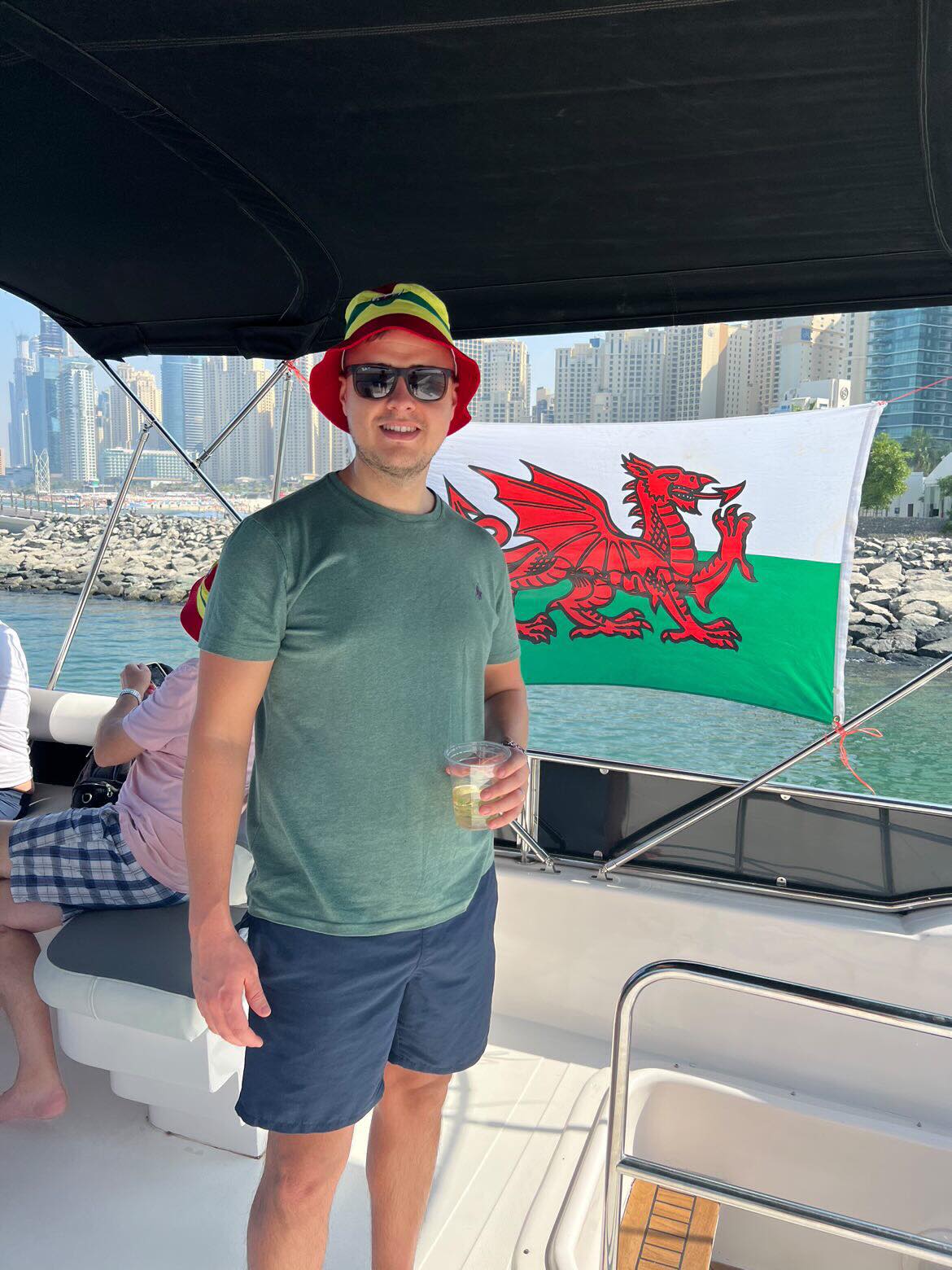 Geraint in New York. Stood on a boat, with the Welsh flag behind him.