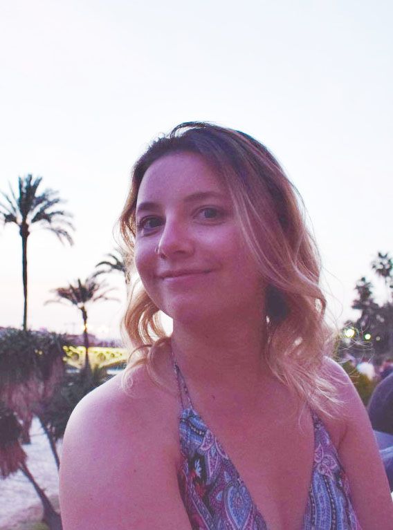Woman in front of palm trees and smiling at the camera.